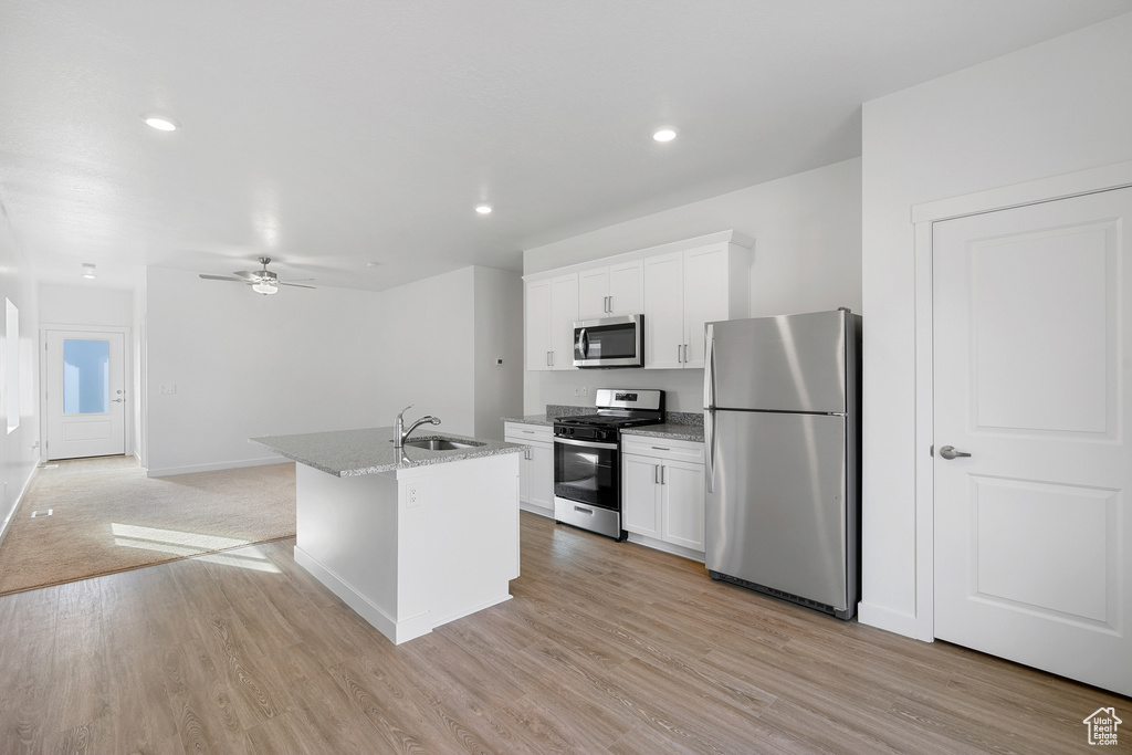 Kitchen featuring appliances with stainless steel finishes, a sink, white cabinetry, an island with sink, and light wood finished floors