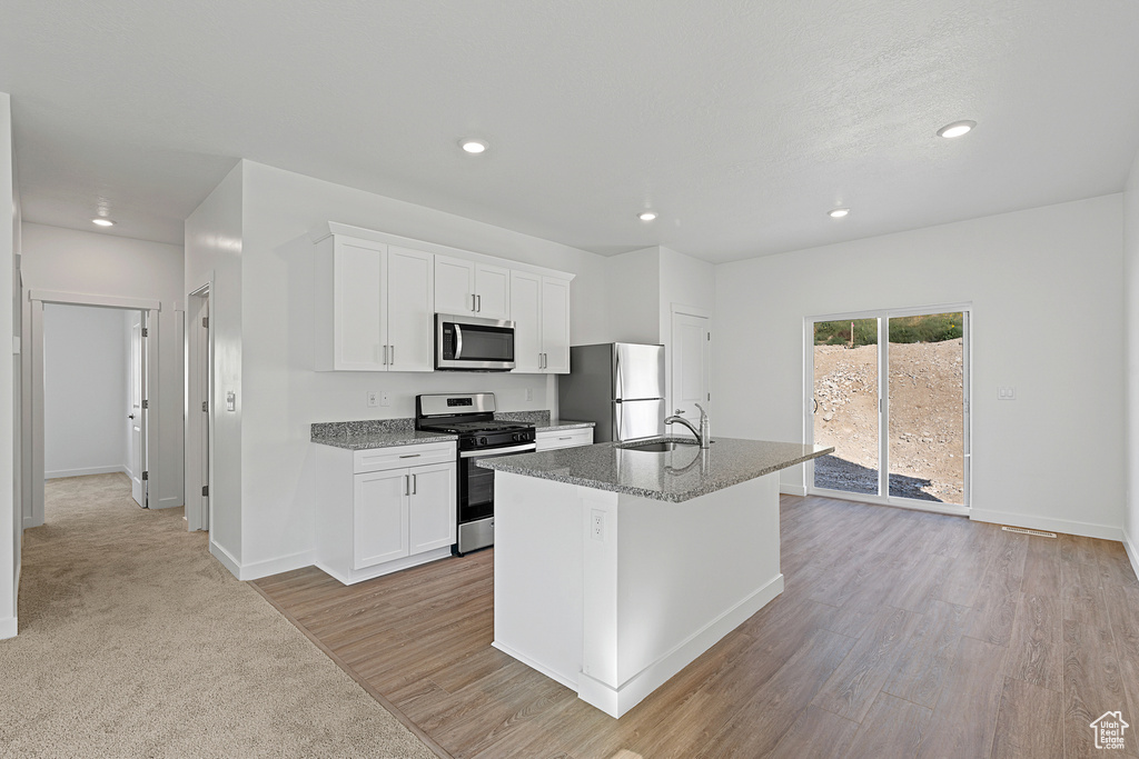 Kitchen featuring stainless steel appliances, a sink, an island with sink, recessed lighting, and white cabinets