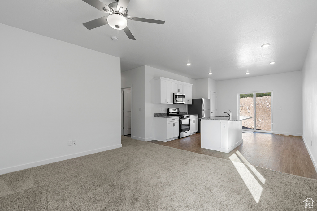 Kitchen featuring stainless steel appliances, a sink, baseboards, a kitchen island with sink, and white cabinets