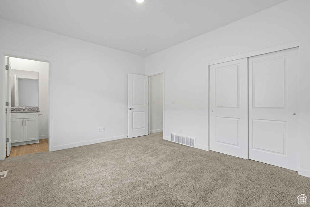 Unfurnished bedroom featuring light carpet, a closet, baseboards, and connected bathroom