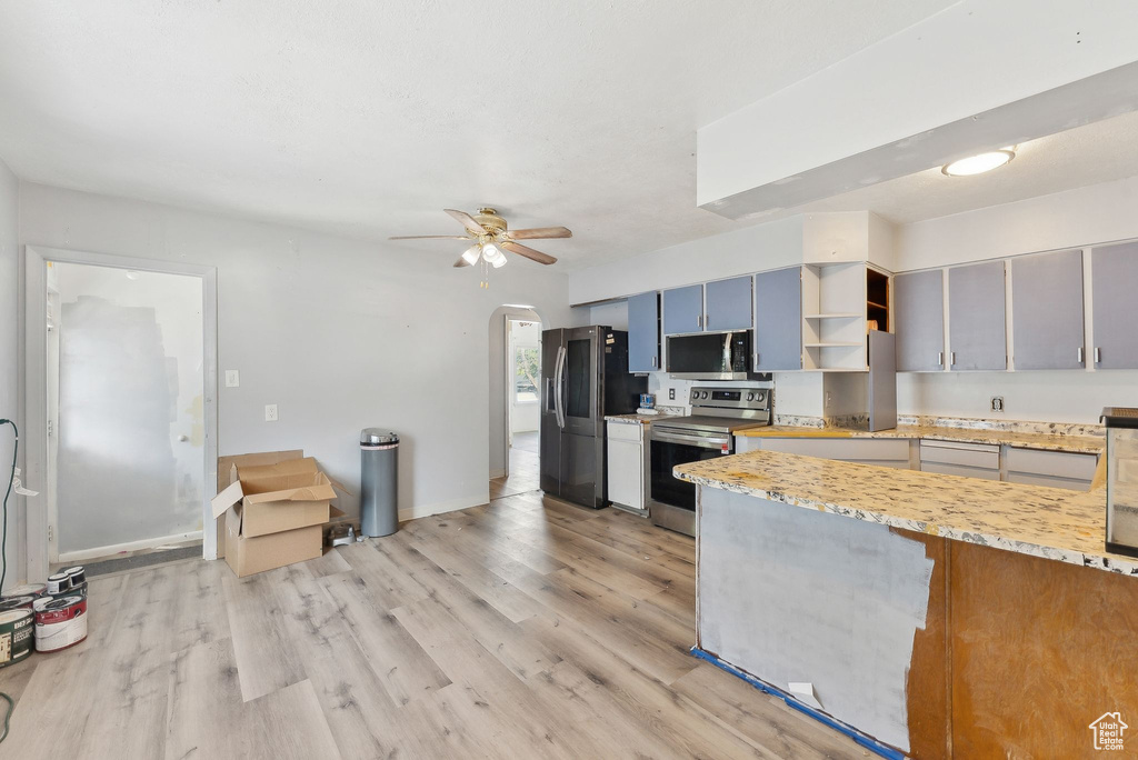Kitchen with appliances with stainless steel finishes, light wood finished floors, arched walkways, open shelves, and ceiling fan
