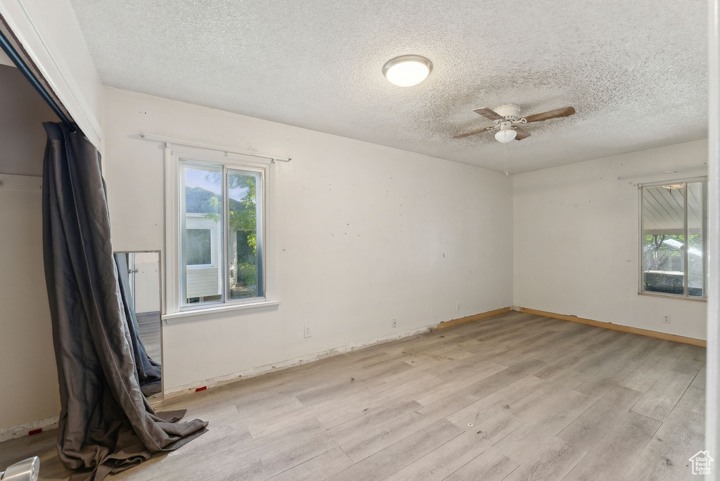 Spare room with light wood-type flooring, a ceiling fan, a textured ceiling, and baseboards