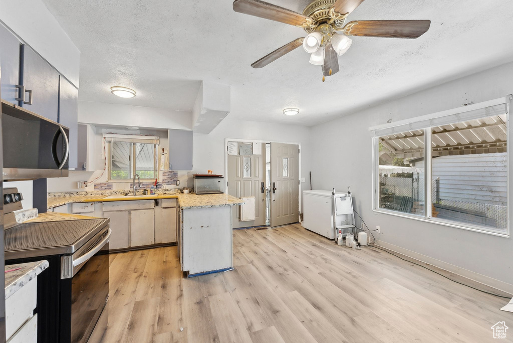 Kitchen featuring a peninsula, range with electric cooktop, light wood-style floors, ceiling fan, and baseboards