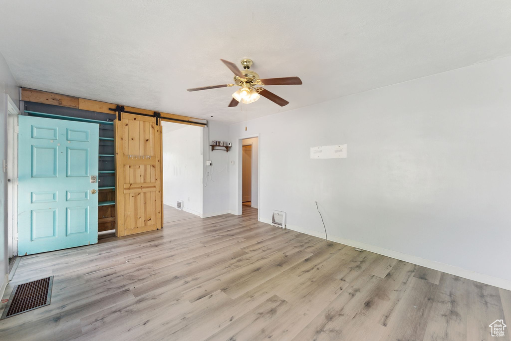 Unfurnished room with a ceiling fan, a barn door, and light wood finished floors