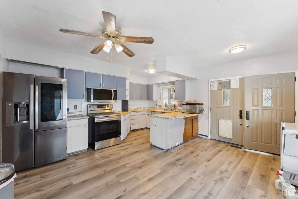 Kitchen with appliances with stainless steel finishes, a peninsula, a ceiling fan, and light wood finished floors