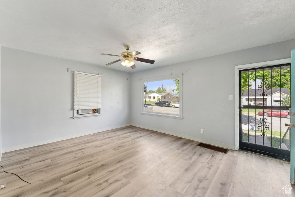 Spare room with ceiling fan, light wood finished floors, baseboards, and a textured ceiling