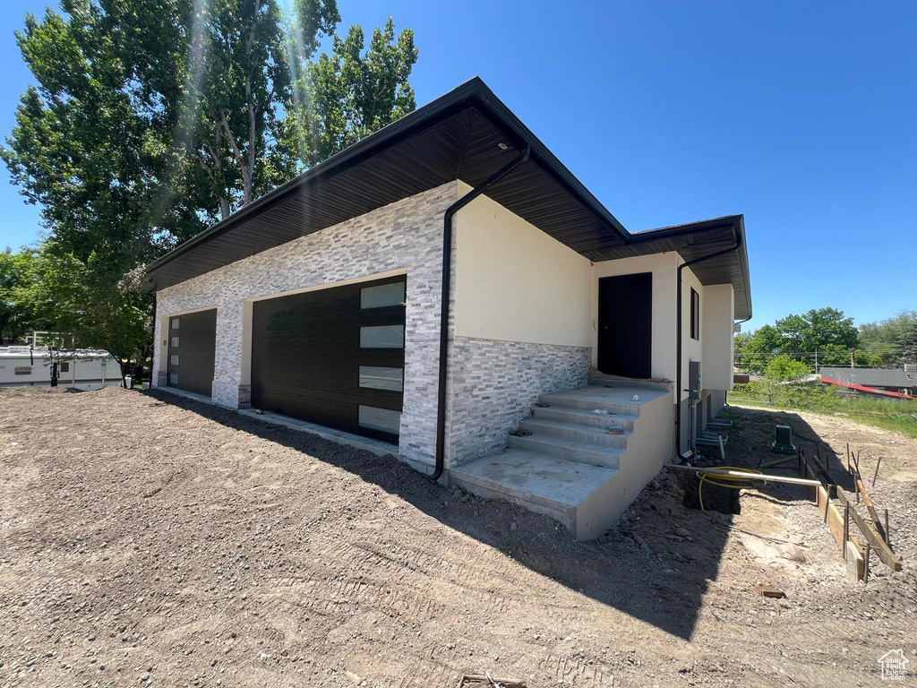 View of side of property with stucco siding, dirt driveway, and stone siding