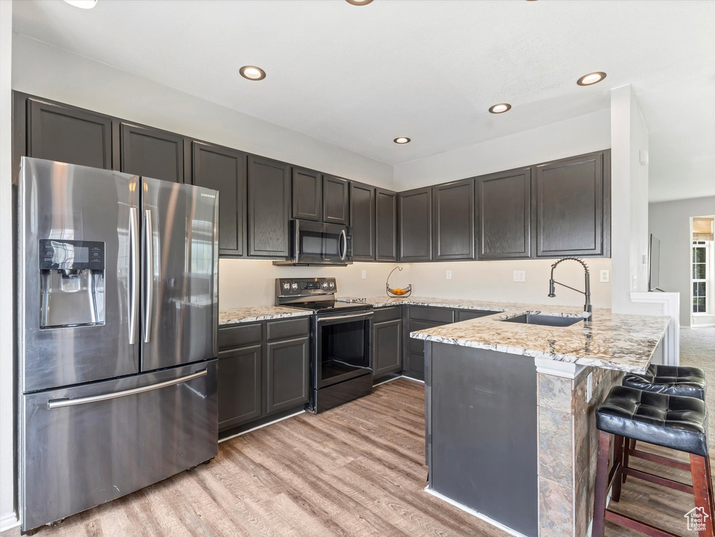 Kitchen featuring stainless steel appliances, a sink, a peninsula, light wood-style floors, and light stone counters