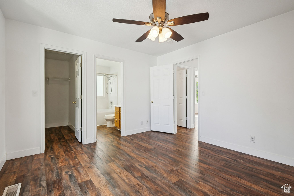 Unfurnished bedroom with a spacious closet, wood finished floors, baseboards, a closet, and ensuite bath