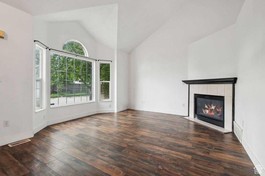 Unfurnished living room featuring wood finished floors, a tile fireplace, high vaulted ceiling, and baseboards