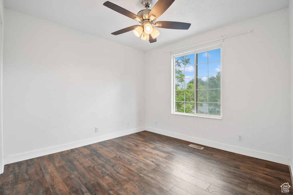 Spare room featuring baseboards, dark wood-type flooring, and a ceiling fan