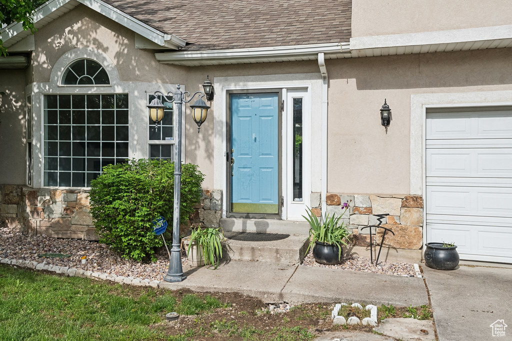 View of exterior entry featuring a shingled roof, stucco siding, stone siding, and a garage