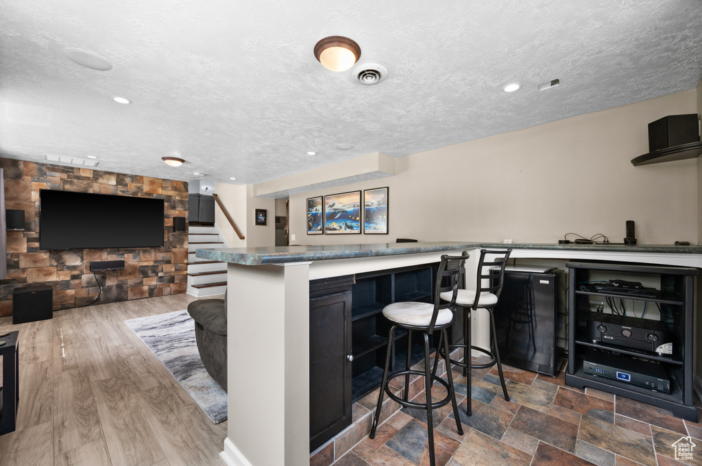 Kitchen featuring a kitchen bar, a textured ceiling, open floor plan, recessed lighting, and dark cabinets