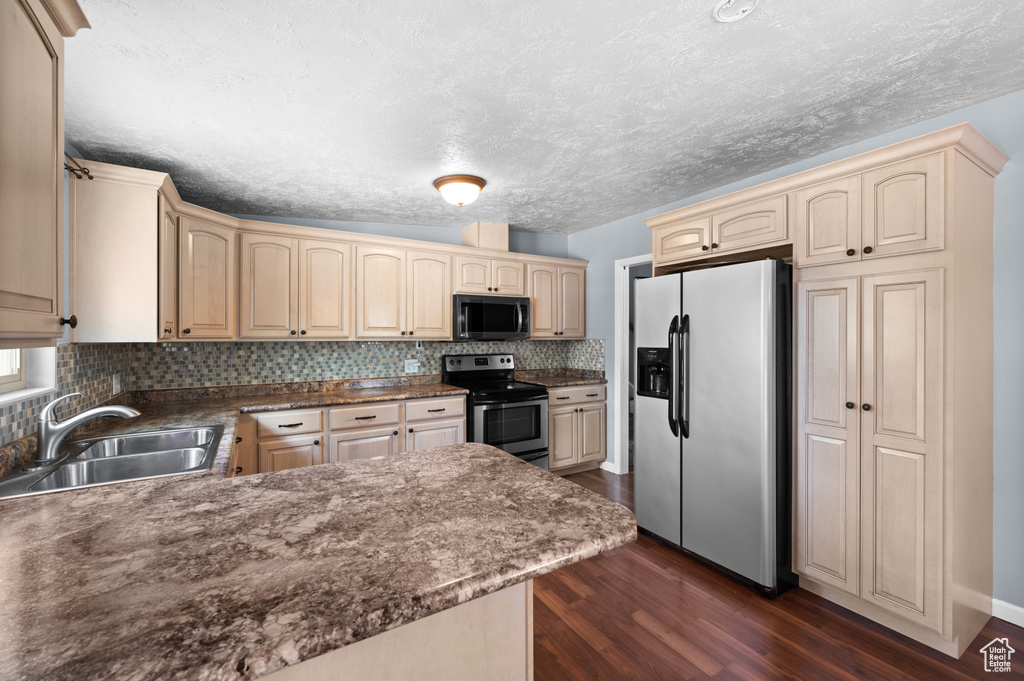 Kitchen with appliances with stainless steel finishes, a sink, cream cabinetry, decorative backsplash, and a textured ceiling