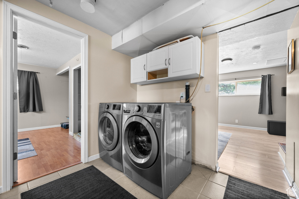Laundry area with washer and dryer, cabinet space, a textured ceiling, light wood-style floors, and baseboards
