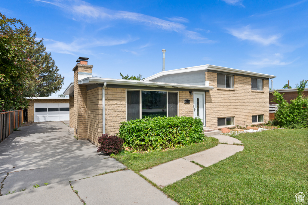 Split level home featuring a chimney, a front lawn, an outdoor structure, and brick siding