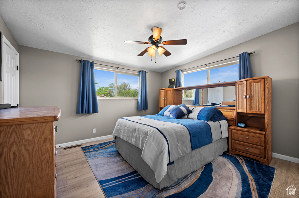 Bedroom featuring multiple windows, baseboards, light wood finished floors, a ceiling fan, and a textured ceiling