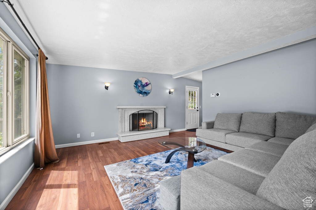 Living room featuring wood finished floors, baseboards, a warm lit fireplace, and a textured ceiling