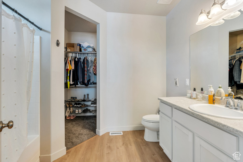 Bathroom featuring wood finished floors, toilet, vanity, baseboards, and a walk in closet