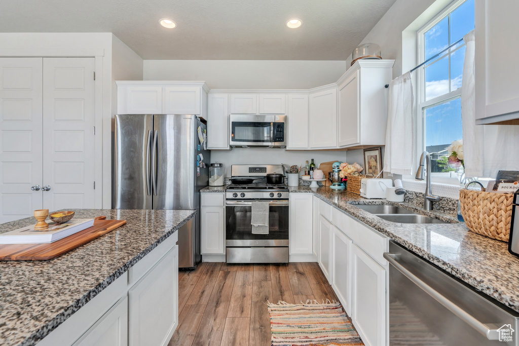 Kitchen featuring appliances with stainless steel finishes, a sink, white cabinetry, light stone countertops, and recessed lighting