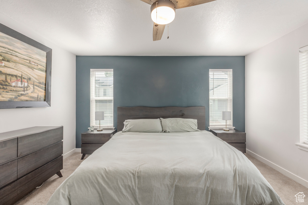 Bedroom with light carpet, multiple windows, baseboards, and a textured ceiling