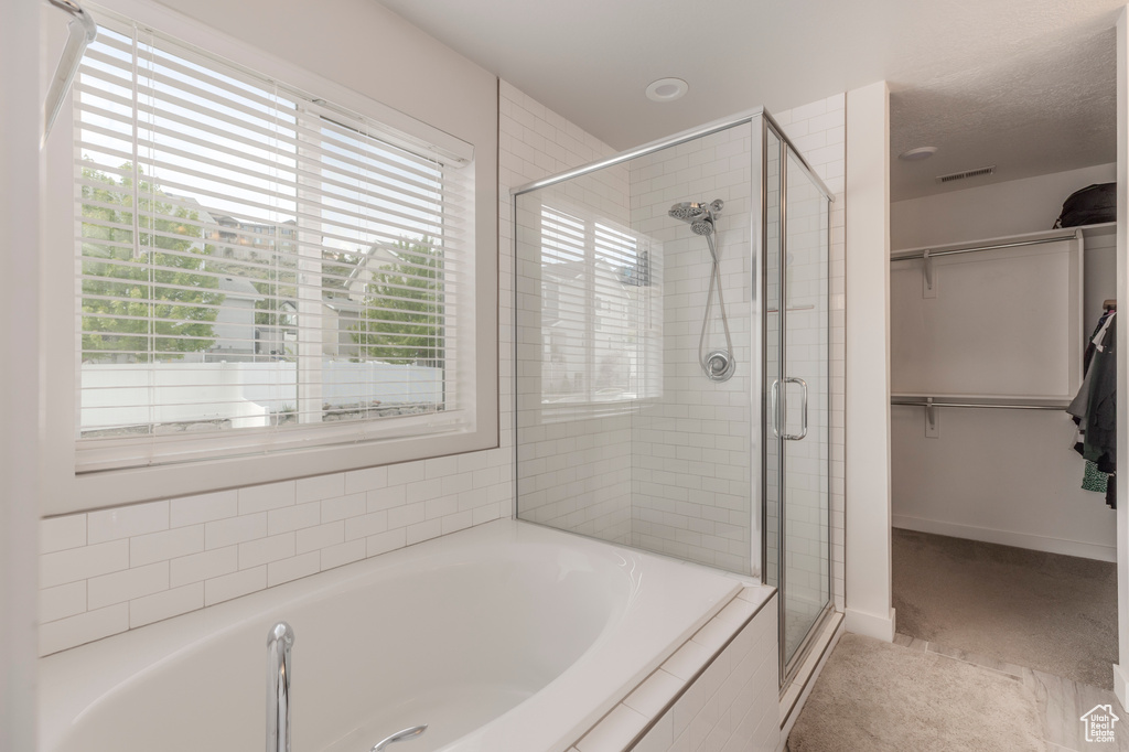 Bathroom featuring a stall shower, a bath, a spacious closet, and baseboards