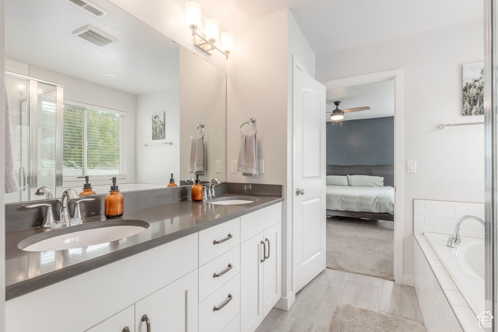 Ensuite bathroom featuring ceiling fan, tiled tub, double vanity, and a shower with shower door