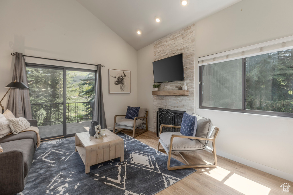 Living area with wood finished floors, a fireplace, high vaulted ceiling, baseboards, and recessed lighting