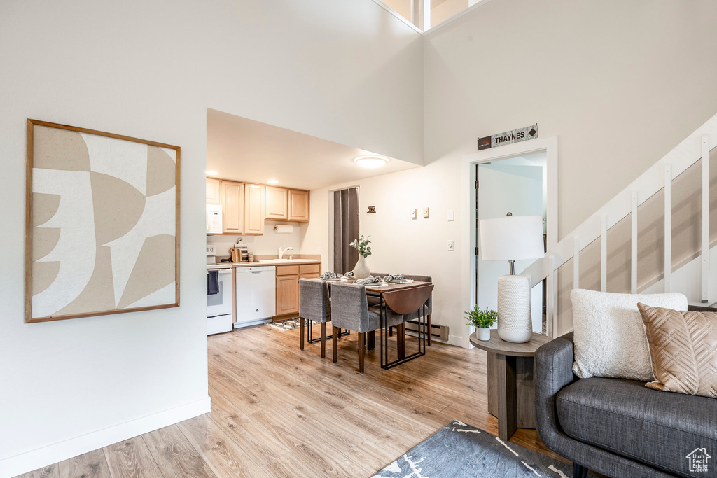 Living area featuring a towering ceiling, light wood-type flooring, a baseboard heating unit, stairs, and baseboards