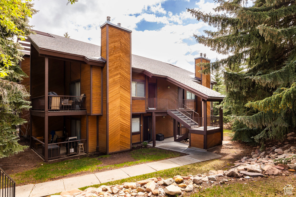 Back of property featuring a chimney, a shingled roof, a balcony, stairway, and a patio area