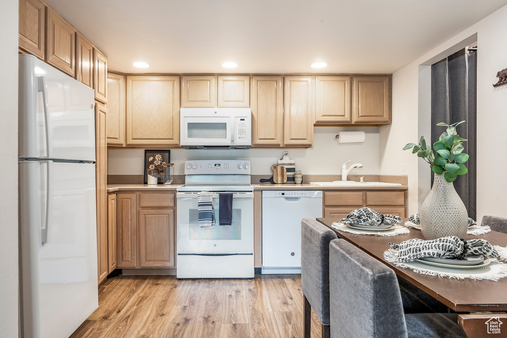 Kitchen with white appliances, a sink, light brown cabinets, light wood-style flooring, and light countertops
