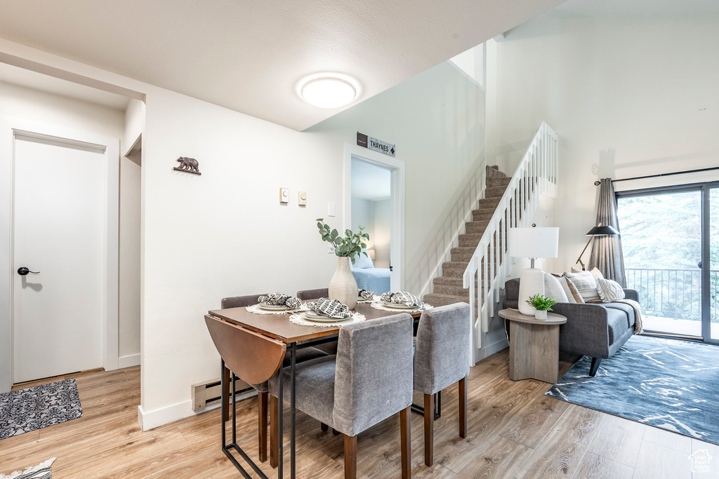 Dining room with light wood finished floors, stairs, a baseboard heating unit, and baseboards