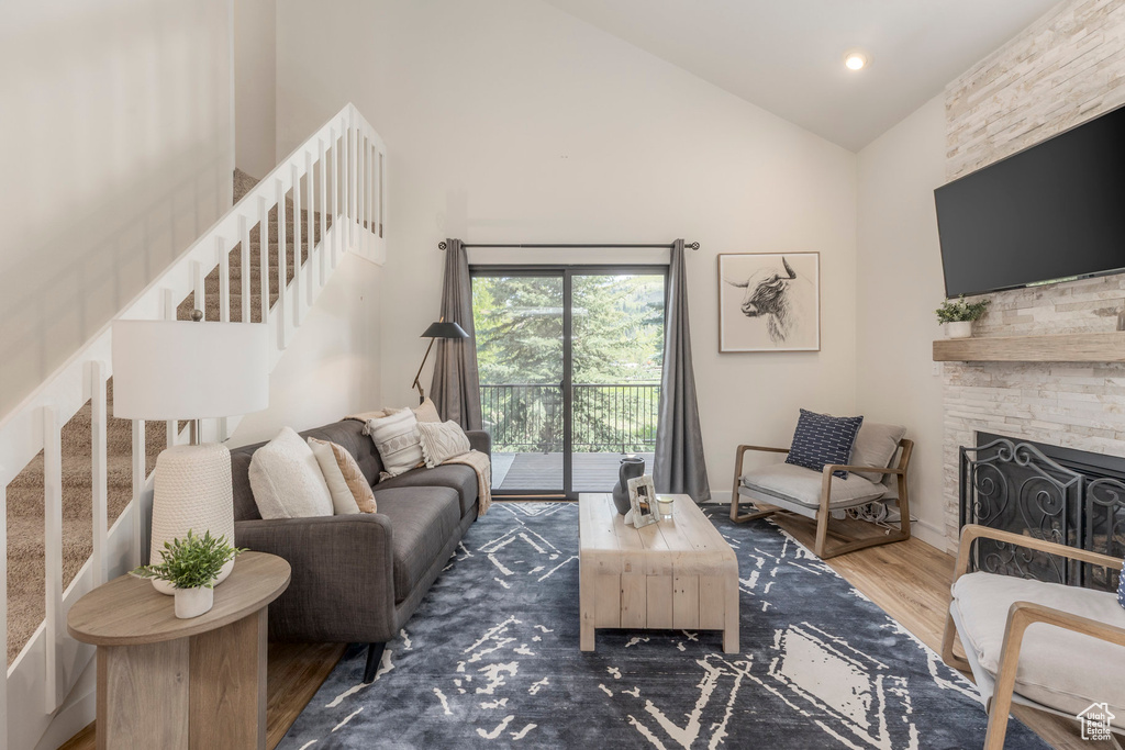 Living area featuring stairs, wood finished floors, high vaulted ceiling, and a fireplace