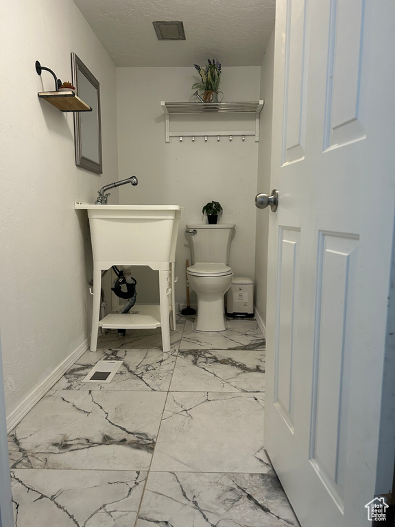 Bathroom featuring marble look tile flooring, toilet, and baseboards