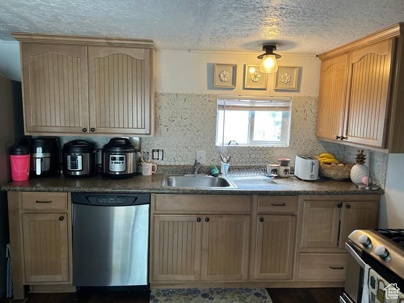 Kitchen with appliances with stainless steel finishes, a sink, dark countertops, backsplash, and a textured ceiling