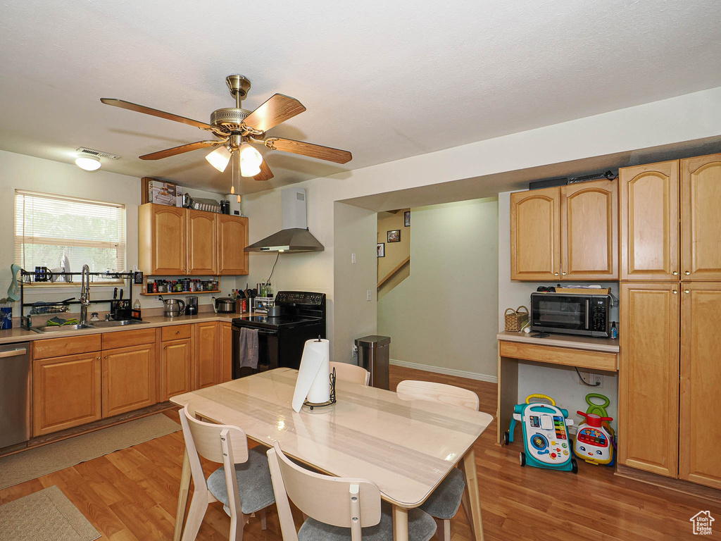Kitchen with wall chimney range hood, black appliances, a sink, light wood-type flooring, and light countertops