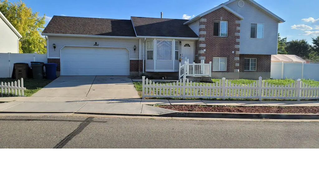 Tri-level home with brick siding, a garage, concrete driveway, and a fenced front yard