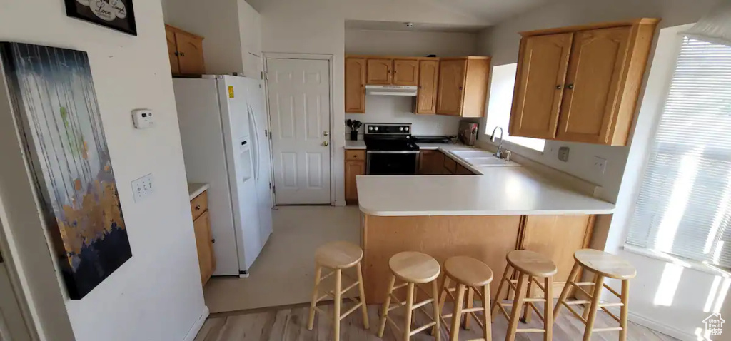 Kitchen with stainless steel range with electric cooktop, white refrigerator with ice dispenser, a sink, a peninsula, and under cabinet range hood