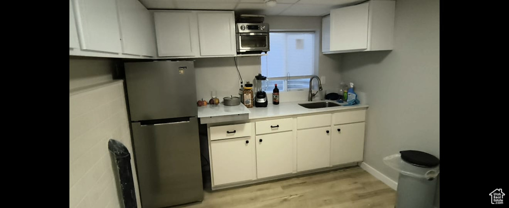Kitchen featuring freestanding refrigerator, a sink, a paneled ceiling, light countertops, and white cabinetry