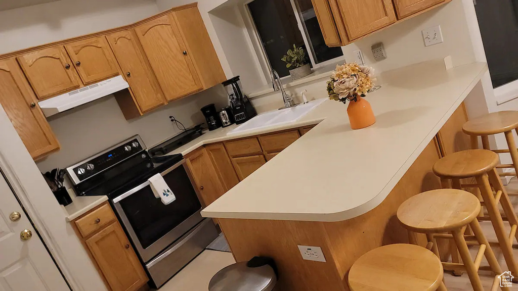 Kitchen featuring stainless steel electric range oven, a breakfast bar area, under cabinet range hood, a sink, and light countertops