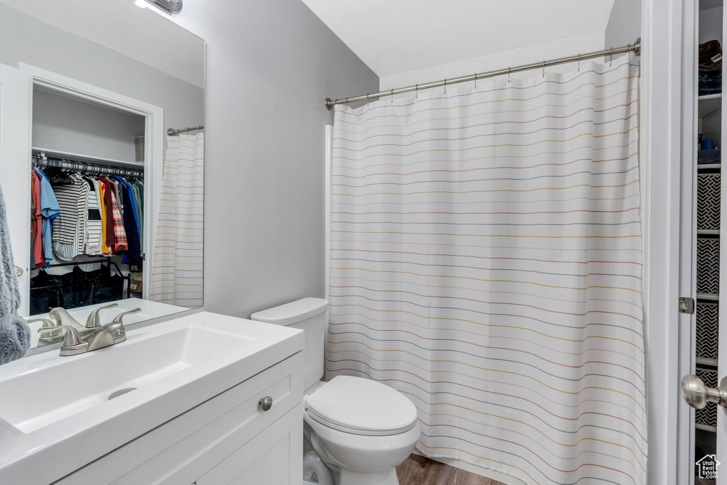 Full bathroom with toilet, vanity, a spacious closet, wood finished floors, and a shower with shower curtain
