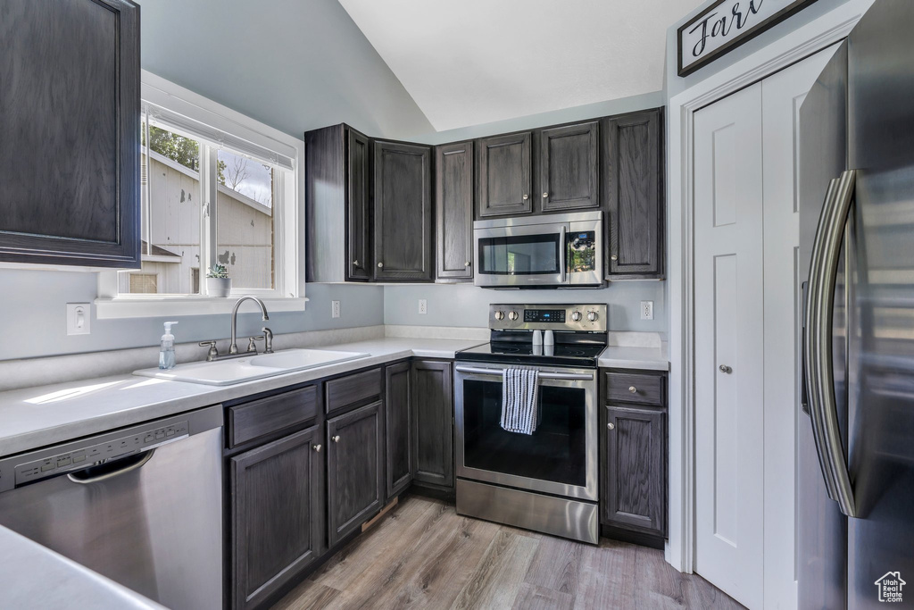 Kitchen featuring stainless steel appliances, a sink, vaulted ceiling, light countertops, and light wood-style floors