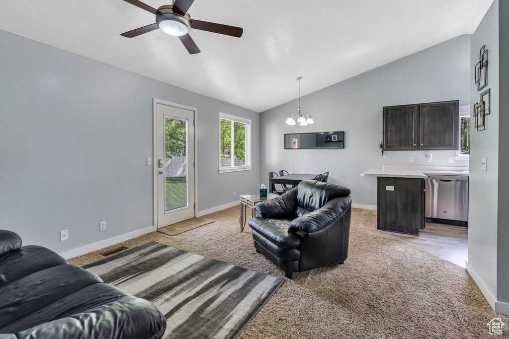Living room with light colored carpet, a chandelier, vaulted ceiling, ceiling fan, and baseboards