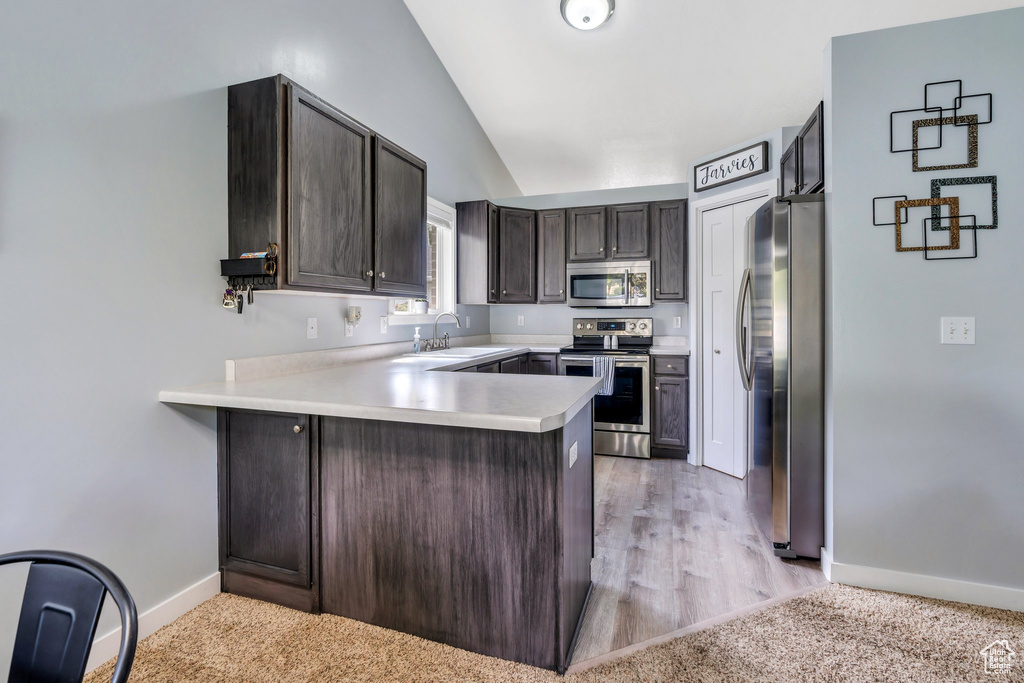 Kitchen featuring stainless steel appliances, lofted ceiling, a peninsula, light countertops, and dark brown cabinets