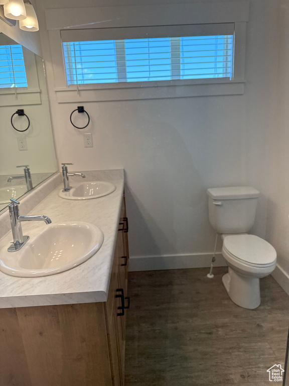 Bathroom featuring baseboards, double vanity, toilet, and wood finished floors