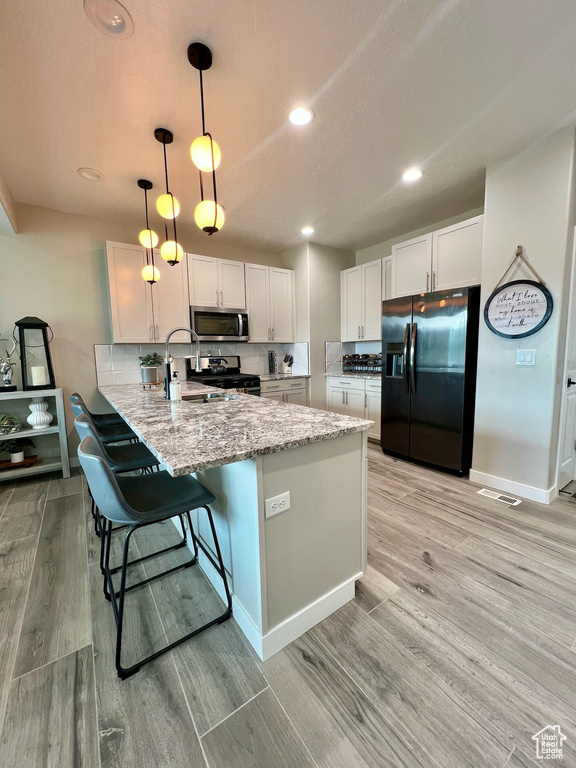 Kitchen featuring stainless steel appliances, a peninsula, light wood finished floors, a sink, and white cabinetry