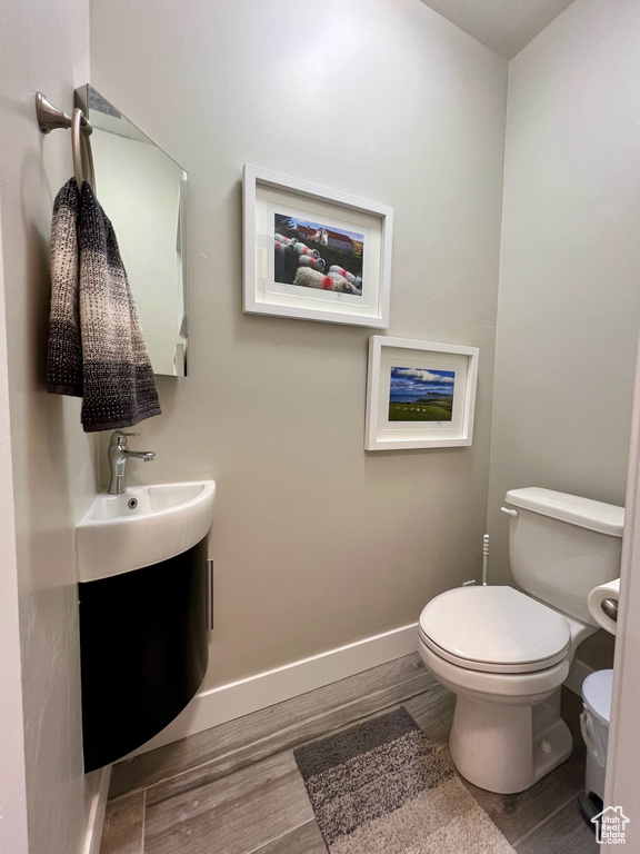 Bathroom featuring wood finished floors, toilet, and baseboards