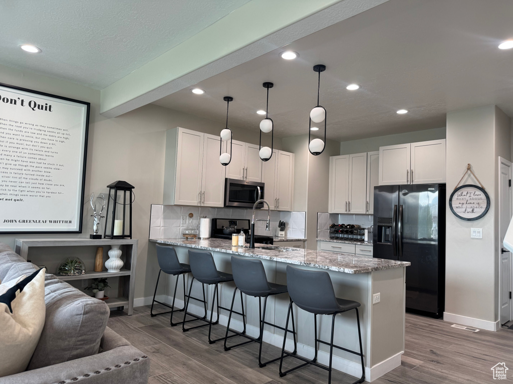 Kitchen featuring a peninsula, black fridge, a kitchen breakfast bar, wood finished floors, and recessed lighting