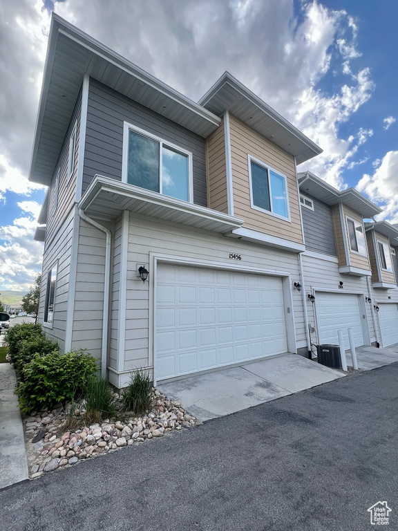 View of front of home with a garage, asphalt driveway, and central AC