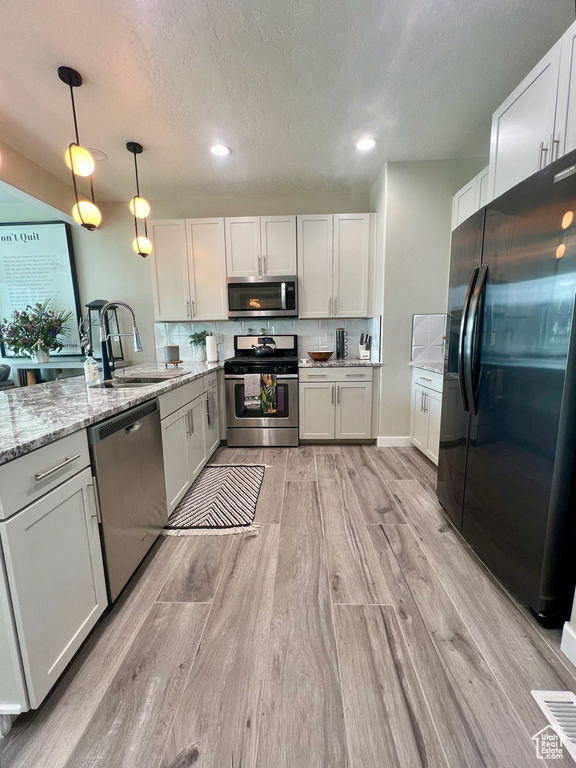 Kitchen featuring stainless steel appliances, a sink, light wood finished floors, light stone counters, and recessed lighting